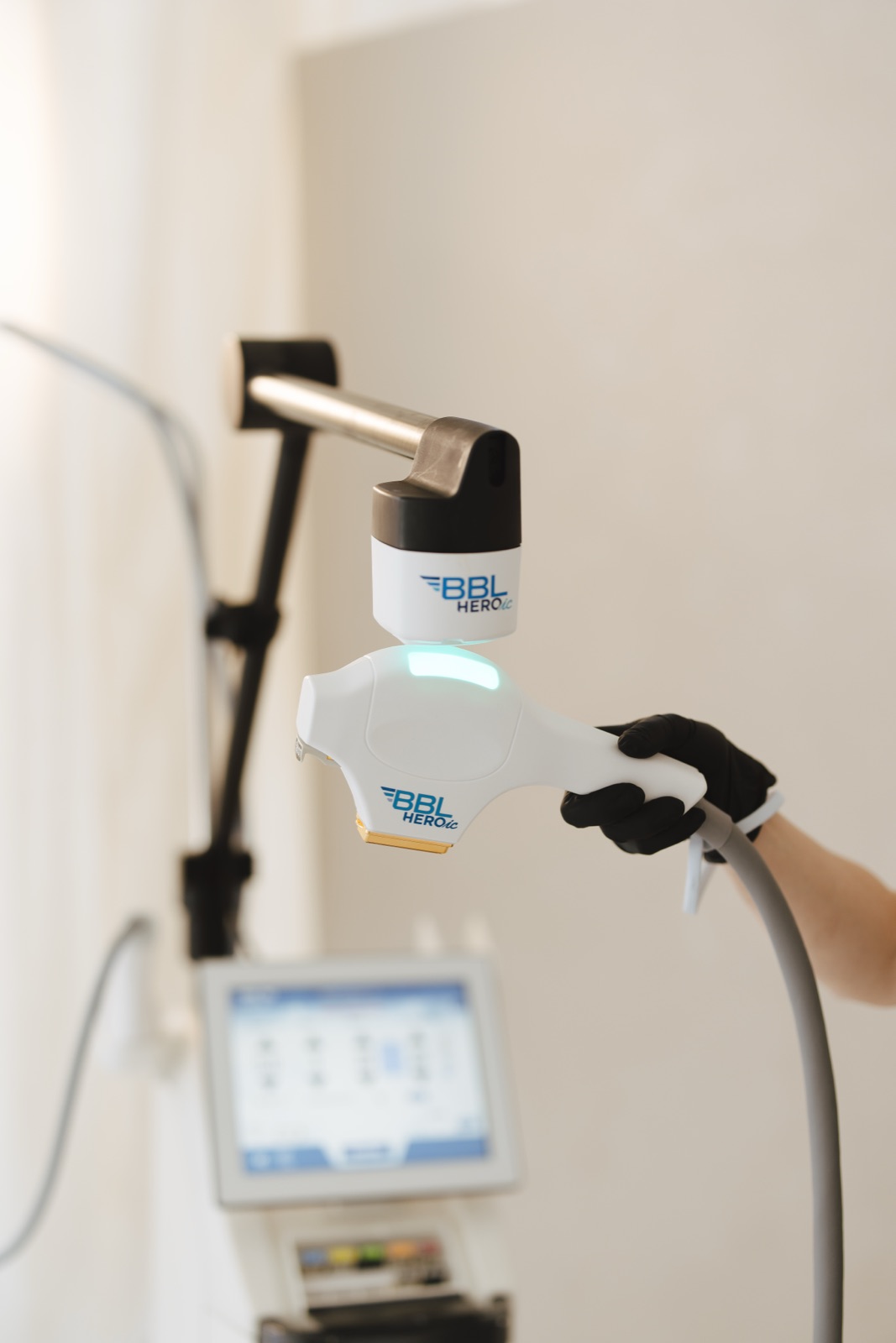 Natalia holds the BBL HEROic broadband light handpiece beside the mJoule platform